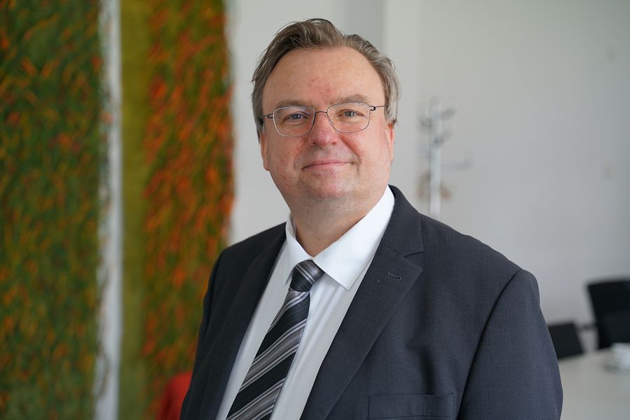 Foto: Professor Haentjens im Portrait. Er trägt Anzug, Krawatte, Brille und blickt in die Kamera. 