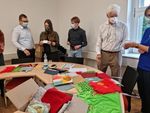 Foto: Mehrere Menschen stehen um einen Tisch auf dem Stoffe liegen.