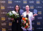 Zwei junge Frauen stehen nebeneinander und haben jeweils einen Preis und einen Blumenstrauß in der Hand.