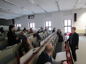 Foto: Teilnehmer sitzen in einem Hörsaal und sind im Gespräch mit einer Referentin. Bild 7
