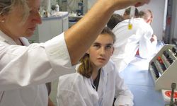 Foto: Eine Schülerin schaut zu wie eine Lehrerin im Reagenzglas eine Flüssigkeit hin und her bewegt.