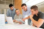 Studienrende und eine Lehrkraft sitzen vor einem Laptop und einem Tablet und diskutieren.