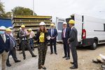 Foto: Mehrere Personen mit Bauhelmen stehen überwiegend lachend in einer Baustellenumgebung.
