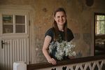 Foto: Eine junge Frau steht mit einem Blumenstrauss lächelnd im Flur eines alten Hauses.