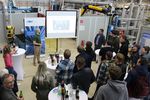 Präsentation in einer Laborhalle. Referenz spricht vor einer Leinwand, Zuhörer stehen und hörenb zu
