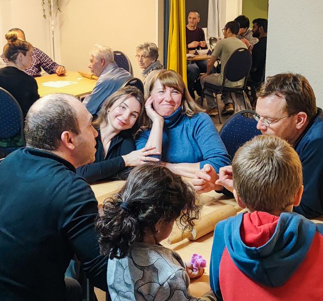 Personen sitzen in einer lockeren Runde in einem Cafe und sprechen miteinander. 