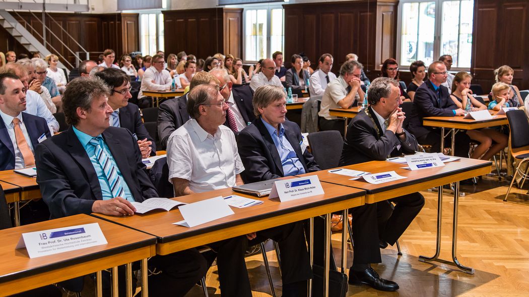 Foto: Teilnehmer sitzen in der Aula und hören einem Vortrag zu.