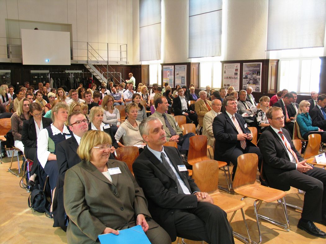 Foto: Teilnehmer sitzen in der Aula und hören einem Vortrag zu.