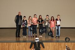 Foto: Ein Gruppe Schülerinnen und ihr Lehrer stehen in der Aula Scheffelberg aufgereiht auf der Bühne. Eine der Schülerinnen hält eine Urkunde hoch.