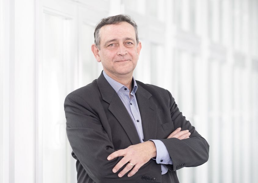 Foto: Ein Mann schaut vor einem verschwommenen Hintergrund in die Kamera. 