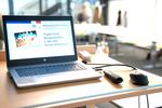 Foto: Ein Laptop mit Anzeige eines Willkommengrußes steht auf einem Tisch.