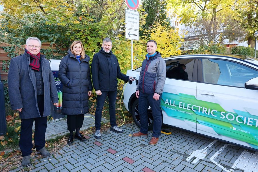 Foto: Projekt E-Com, Projektpartner vor E-Ladesäule und einem Elektrokraftfahrzeug, welches geladen wird