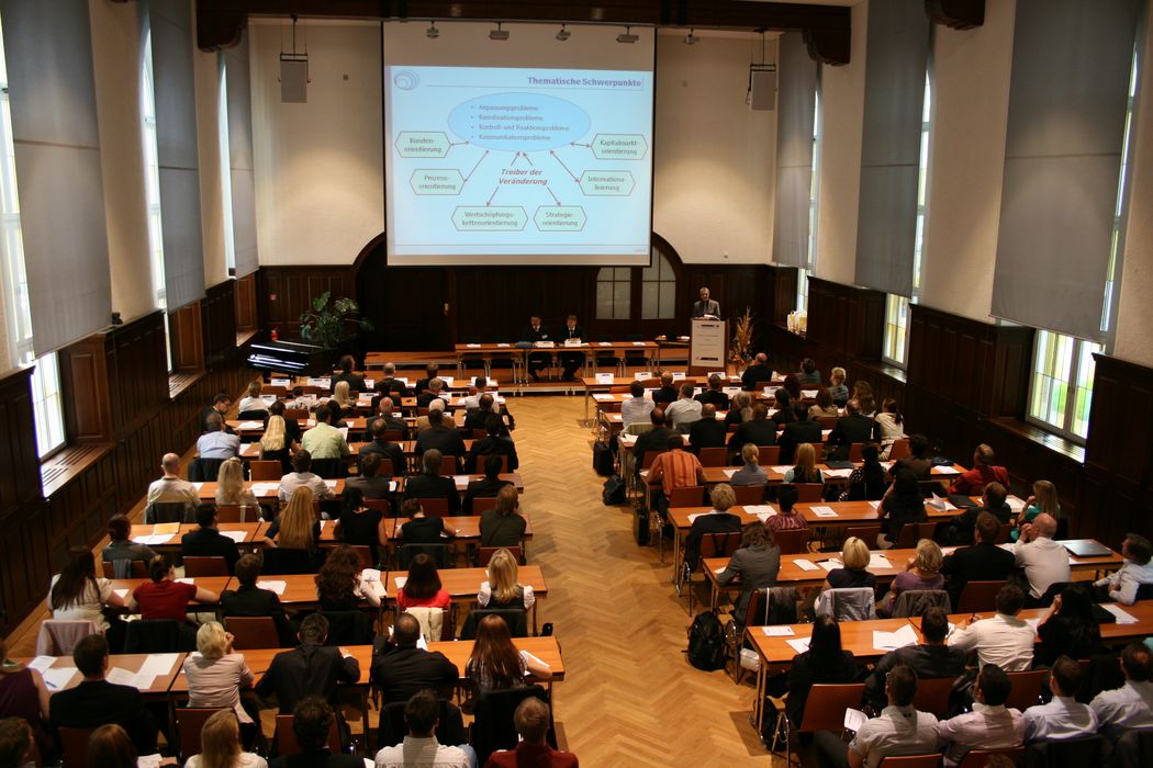 Foto: Teilnehmer sitzen in der Aula und hören einem Vortrag zu.