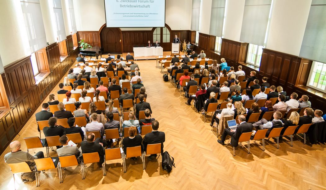Foto: Teilnehmer sitzen in der Aula und hören einem Vortrag zu.