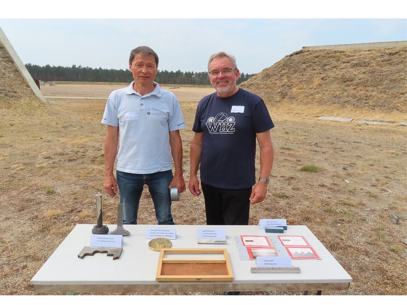 Mitarbeiter und Professor stehen auf einem Testgelände vor einem Tisch und blicken in die Kamera