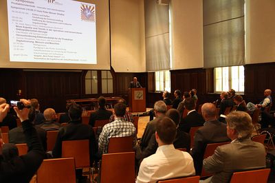 Foto: 6. Symposium 2017. Ein Redner hält in der Aula vor den Teilnehmern einen Vortrag.