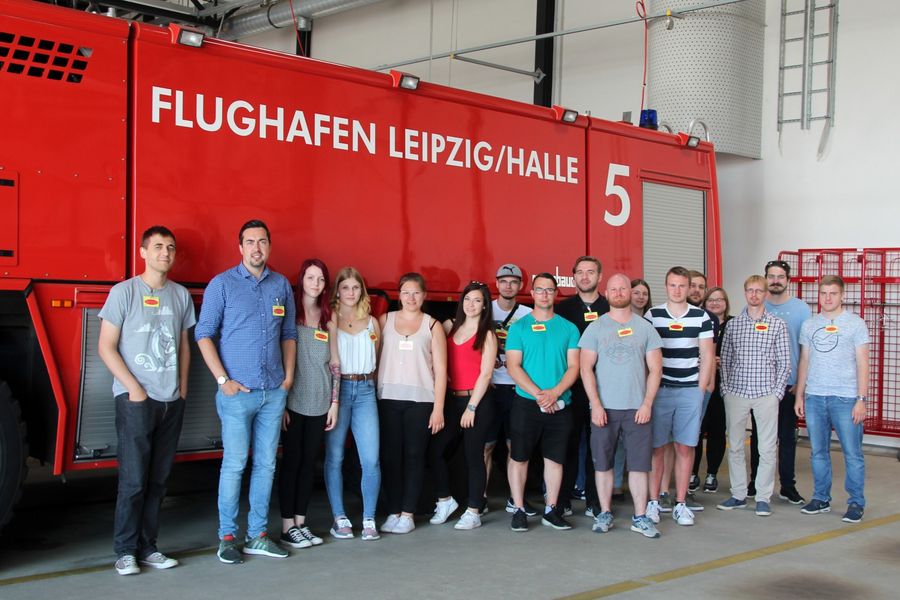 Foto: Gruppenbild vor einem Löschfahrzeug der Flughafenfeuerwehr.