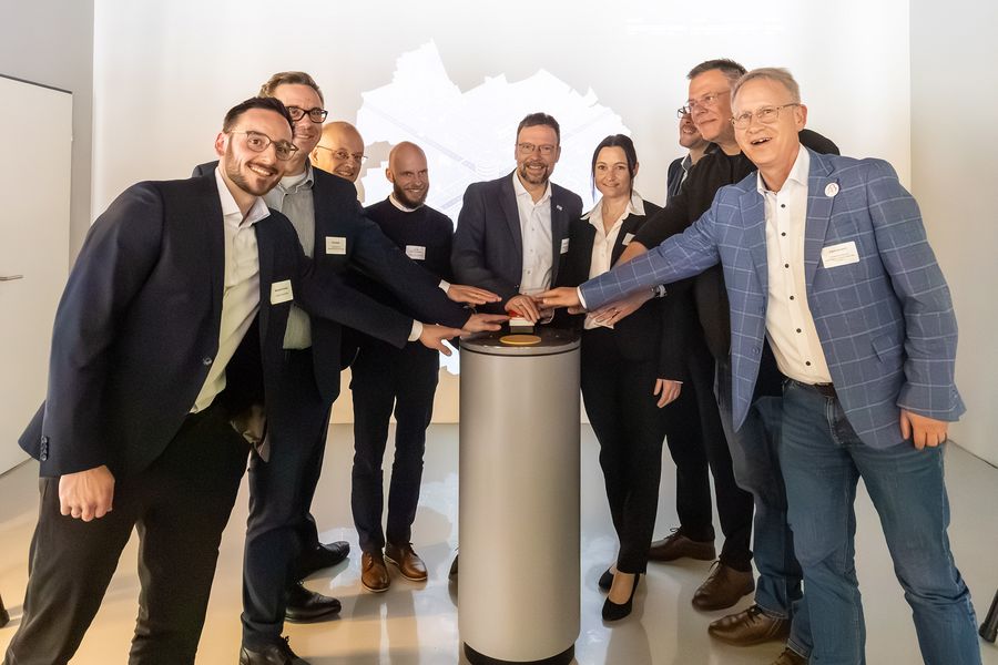 Eine Gruppe von Menschen drückt gemeinsam einen großen Knopf. Dies steht symbolisch für den Start der Ausstellung. 
