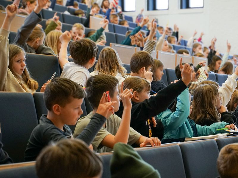 Kinder sitzen in einem Hörsaal und melden sich. 