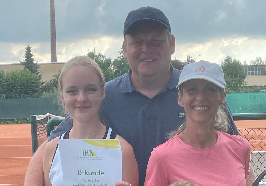 Mike Espig stehend auf einem Tennisplatz, Blick in die Kamera, vor ihm seine Familie, ein Kind hält die Urkunde in der Hand. 