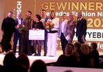 Eine Gruppe von Personen steht auf einer hell erleuchteten Bühne, im Hintergrund der Schwirftzug "Gewinner"
