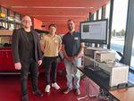 3 Personen stehen vor einem Monitor und einem Messgerät und blicken in die Kamera.