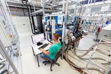 Ein Mitarbeiter sitzt am Rechner in der Prüfstandshalle und bedient den Wärmeübertragerprüfstand, der neben ihm steht (Quelle: WHZ)