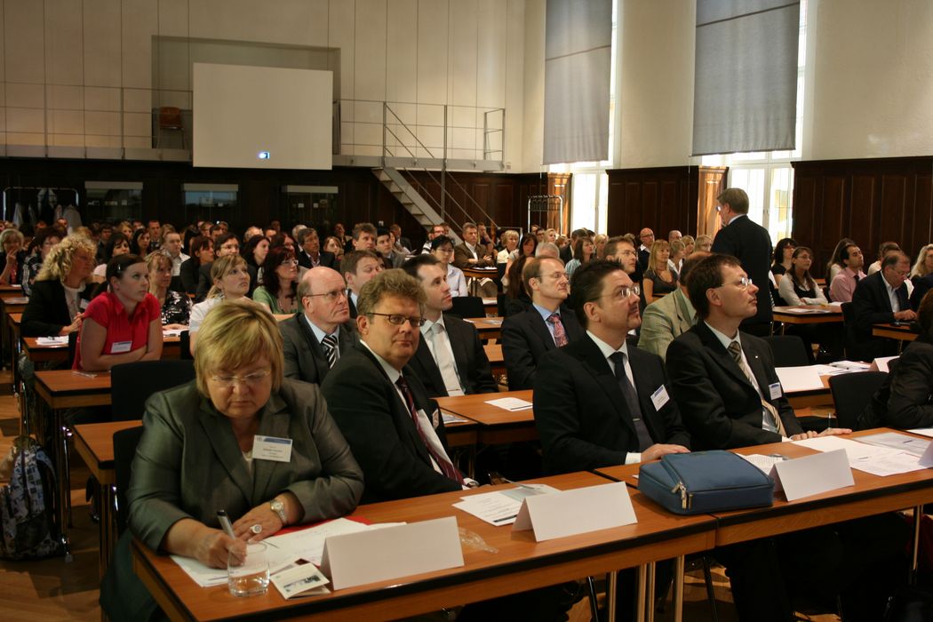 Foto: Teilnehmer sitzen in der Aula und hören einem Vortrag zu.