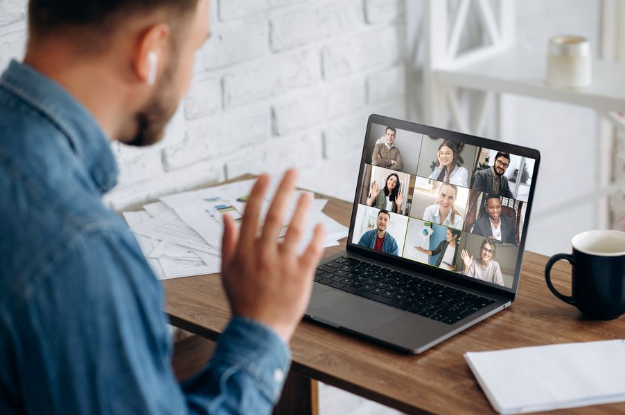 Foto: Ein Mann sitzt vor seinem Laptop. Auf dem Bildschirm 9 Personen zu einer Videokonferenz.