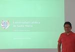 Mann im roten T-Shirt steht vor einer grünen Leinwand mit dem Logo der Santa Maria Universität aus Peru