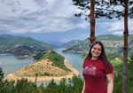 Studierende im Hochschulshirt blickt in Kamera, im Hintergrund Flusslandschaft