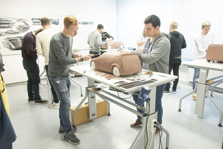 Foto: Studierende stehen an Tischen und modellieren die Modelle von Fahrzeugen.