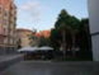 Foto: Blick auf einen kleinen Platz mit anliegenden Grünstreifen und Freisitz eines Restaurant mit Gästen.