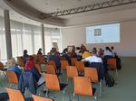 In einem halbrunden Konferenzraum sitzen mehrere Menschen und schauen auf eine Präsentation auf der Wand, auf der das Bild einer Lunge zu sehen ist.