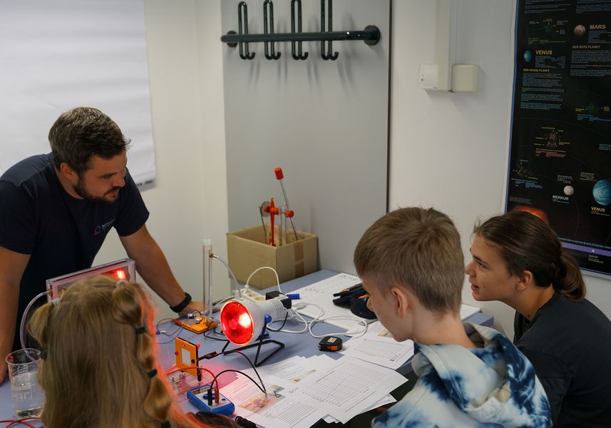 drei Schüler sitzen an einem Tisch und experimentieren gemeinsam mit einem Laboringenieur