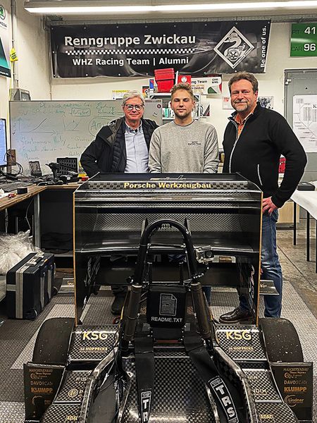 Mr. Ewing, Prof. Schubert und der Team Manager des Racing-Teams Moritz Fischer stehen zum Gruppenbild hinter dem Weltmeisterauto 2023