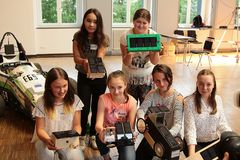 Foto: Sieben Schülerinnen hockend und stehend präsentieren ihre Solar Modellautos.