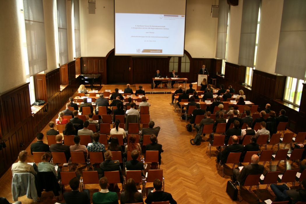 Foto: Teilnehmer sitzen in der Aula und hören einem Vortrag zu.