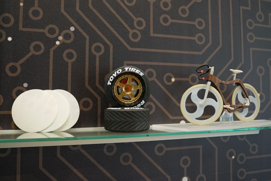 Auf dem Foto ist ein Teil der Ausstellung des 3D-Drucks zu sehen. Abgebildet sind zwei Miniatur-Autoreifen sowie ein Fahrrad.