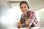 Foto: Eine Frau sitzt mit Headset am Schreibtisch und lächelt in die Kamera.