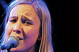 Foto: Jule, Malischke mit Mikrofon und Gitarre. 11. "Talk in der Galerie" sowie Livekonzert von Jule Malischke, Adrian Zendeh und Isabell Kimmel.