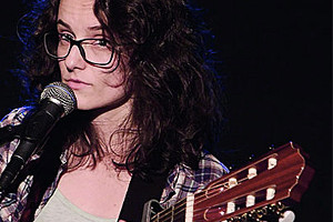 Foto: Livekonzert mit MIRIAM SPRANGER. Steht am Mikrofon mit Gitarre.