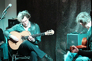 Foto: Neujahrskonzert in der Galerie. Zwei Männer spielen sitzend auf Gitarren.