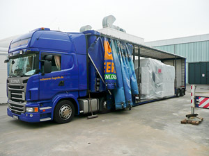 Foto: Seitlicher Blick auf einen LKW. Auf dem Hänger eine neue Werkzeugmaschine.