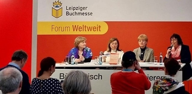 Foto: Vier Frauen an Tisch mit Mikrofon vor Teilnehmern.