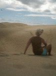 Foto: Eine Sanddüne und eine sitzende Frau.
