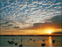 Foto 1: Boote ankern im Wasser. Dahinter ein Sonnenuntergang.