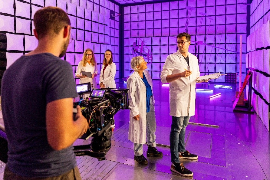 Foto: Personen mit Kitteln in einem futuristischen Raum werden gefilmt