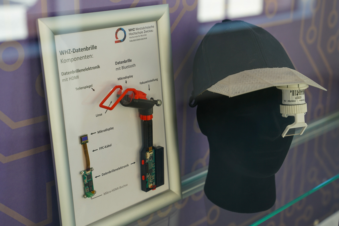 Auf dem Foto sieht man sowohl ein Schaubild zur Datenbrille als auch einen schwarzen Styroporkopf mit Basecap, an dem die Datenbrille angebracht ist.
