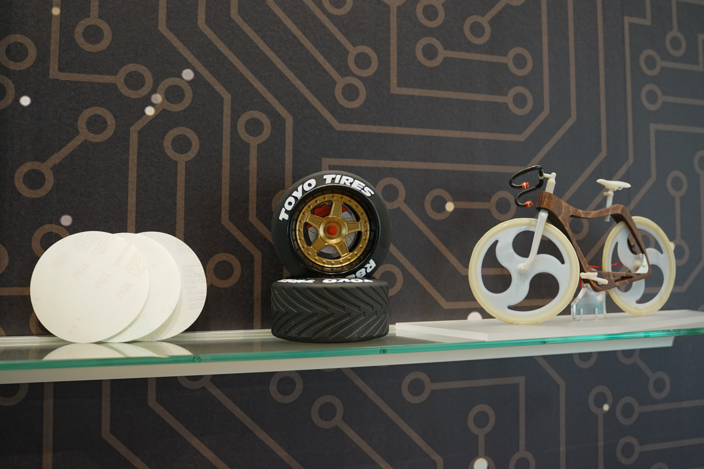 Auf dem Foto ist ein Teil der Ausstellung des 3D-Drucks zu sehen. Abgebildet sind zwei Miniatur-Autoreifen sowie ein Fahrrad.
